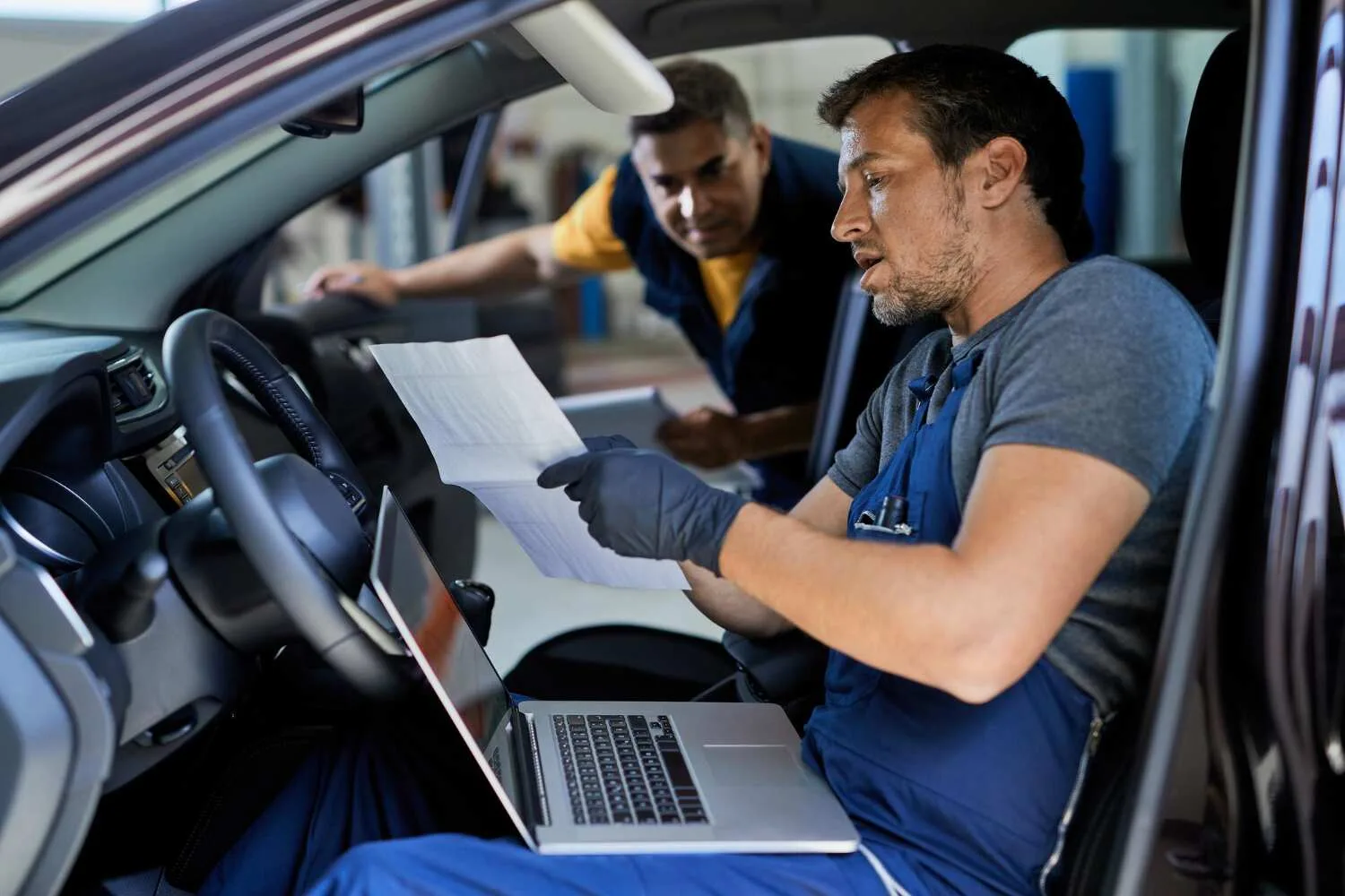 Car AC repair technician checking vehicle system with laptop and service document inside a car in Kuwait workshop.